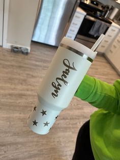 a person holding up a cup with the word vegan on it in front of a kitchen