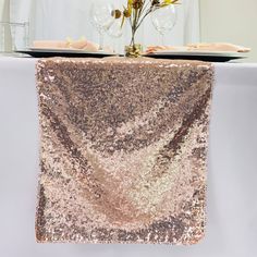 a sequin table runner on top of a white table with wine glasses and flowers