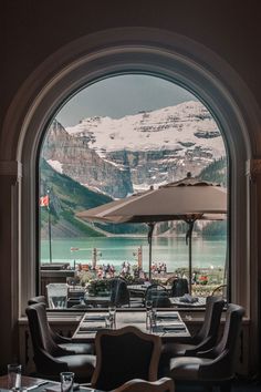 an outdoor restaurant with tables and umbrellas in front of a mountain lake filled with snow