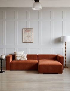 an orange couch sitting on top of a hard wood floor next to a white wall