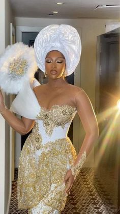 a woman in a white and gold dress is holding a feathered fan while standing next to a doorway