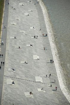 an aerial view of people walking and sitting on the sidewalk next to the water's edge