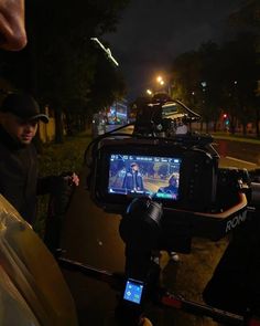 a man holding a video camera in front of a car on the street at night