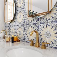 a bathroom with blue and white tiles on the wall, gold faucets and mirrors