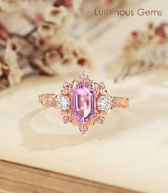 a ring with an oval cut pink sapphire surrounded by smaller round diamonds on top of a book