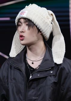 a young man wearing a white knitted hat and black jacket with his tongue out