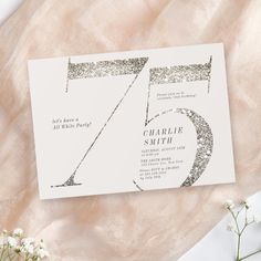 a white and silver wedding card with the number 75 printed on it next to flowers