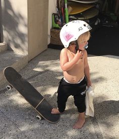 a young boy standing next to a skateboard and talking on a cell phone while wearing a helmet