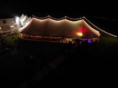 a large tent is lit up at night with lights on the side and people standing outside