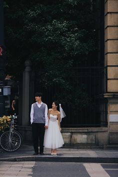 a bride and groom standing on the street in front of an iron gate holding hands