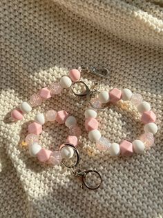 two bracelets with pink and white beads are sitting on a knitted surface next to each other