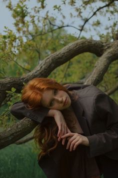 a woman with red hair leaning on a tree branch