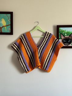 an orange and black crocheted sweater hanging on a wall next to two pictures