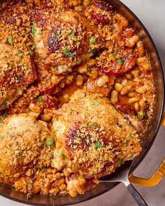 chicken and beans in a skillet with a yellow spatula next to it on a white surface