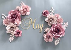 paper flowers with the word may spelled in gold lettering on a gray background, surrounded by leaves and branches