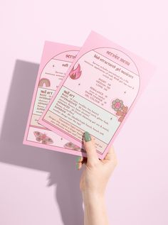 a person holding up two pink menus on top of a table next to each other