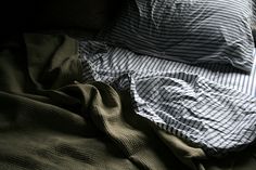 an unmade bed with striped sheets and pillows