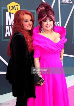 two women in pink dresses standing next to each other on the red carpet at an awards event