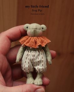 a small teddy bear with an orange dress on it's chest is held in someones hand