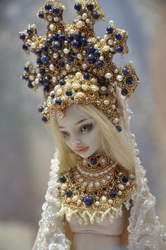 a doll wearing a crown with pearls and blue beads on it's head is shown