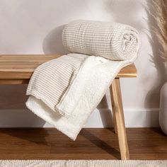 a white blanket sitting on top of a wooden bench next to a vase with dry grass