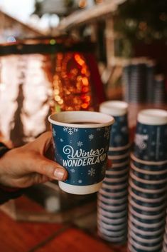 a person holding up a coffee cup in front of stacks of plates