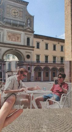 two people sitting on chairs in front of a building with a clock tower behind them