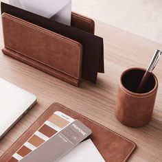 a desk with a pen holder, cup and laptop computer on top of it next to a mouse pad