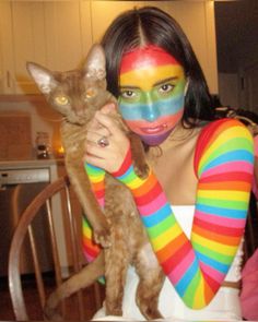 a woman with her face painted like a cat and holding a cat in her arms