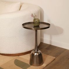 a small table with a vase on it sitting in front of a white couch and rug