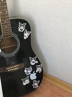 an acoustic guitar with stickers on it sitting in front of a white wall and wooden floor