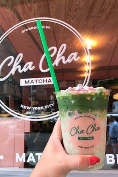 a person holding up a drink in front of a store window with the words cha cha on it