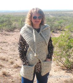 a woman standing in the desert wearing a sweater with hood and leopard print scarf around her neck