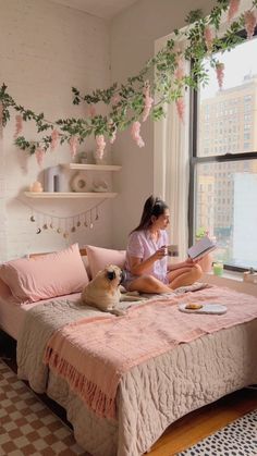 a woman sitting on her bed reading a book next to a dog laying on the bed