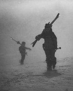 two people walking through the water with skis on their back