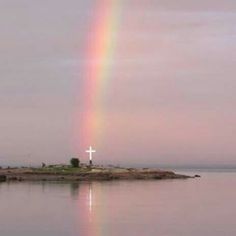 a rainbow shines brightly in the sky over a small island with a cross on it