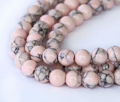 two strands of pink and black marble beads on a white surface with one strand in the middle