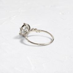 a white gold ring with a pear shaped diamond in the center on a plain surface