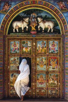 a woman is standing in front of an ornate door with paintings on the doors and walls