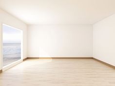 an empty room with wooden floors and white walls, overlooking the ocean on a sunny day