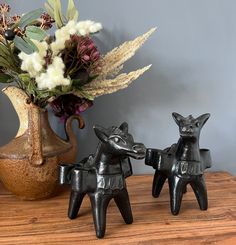 two small metal horses on a wooden table next to a vase with flowers in it