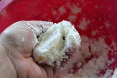 a hand is holding some food in a red bowl with powdered sugar on it