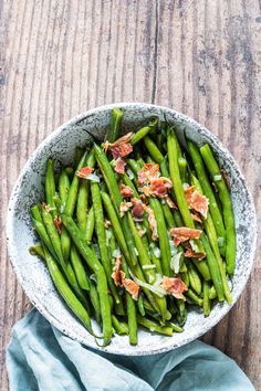 a bowl filled with green beans and bacon on top of a blue cloth next to a wooden table