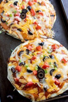 two pizzas sitting on top of a pan covered in cheese and black olives