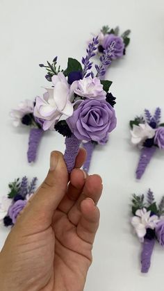 a hand is holding a purple and white boutonniere with flowers on it