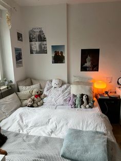 a bed with stuffed animals on it in a bedroom next to a lamp and pictures