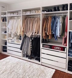 an organized closet with clothes and shoes on the shelves in front of white shelving