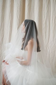 a woman in a wedding dress with a veil on her head sitting down and looking off to the side