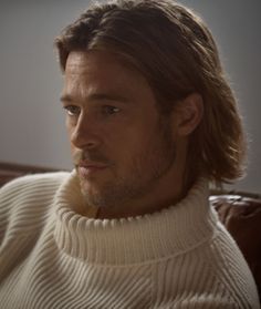 a man with long hair wearing a sweater looking off to the side while sitting on a couch