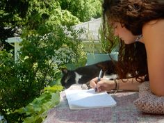 a woman writing on a notebook with a cat in the background